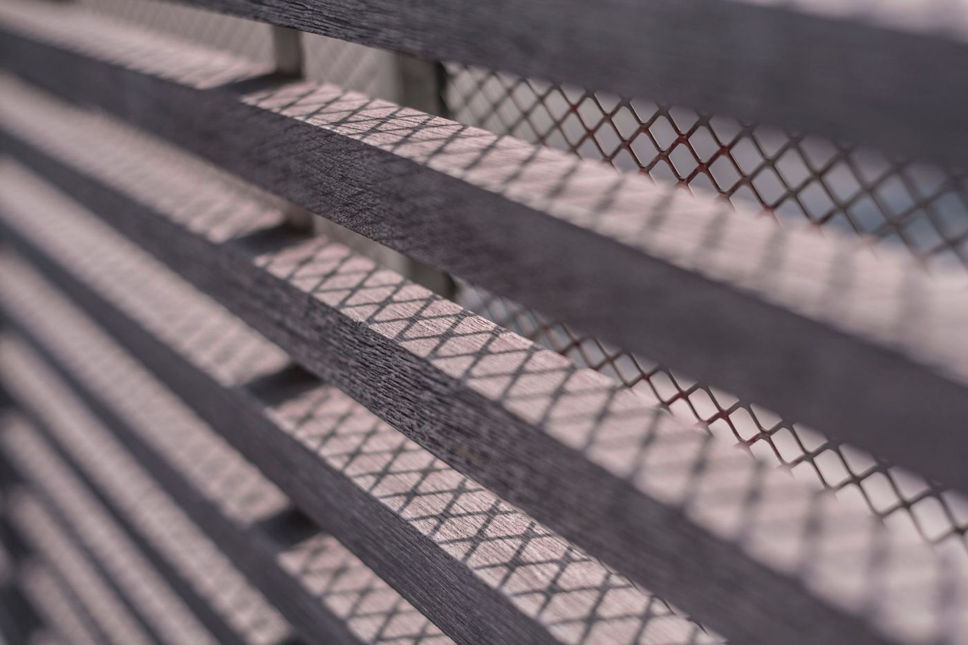 Close-up of dark horizontal fence slats with diamond metal mesh casting a lattice of shadows across them