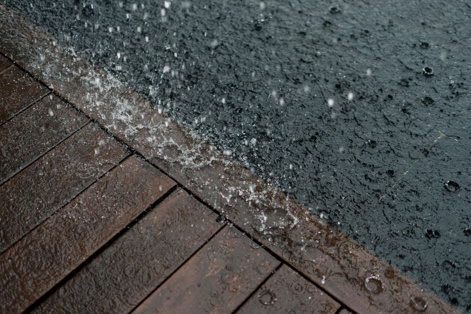 Heavy rain splashing on dark wet deck boards at the edge of a rippling grey surface of water